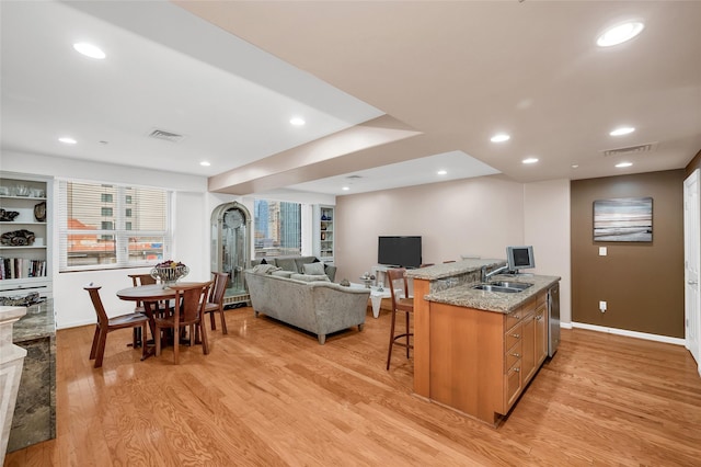 kitchen with light stone counters, a sink, a kitchen breakfast bar, open floor plan, and light wood finished floors