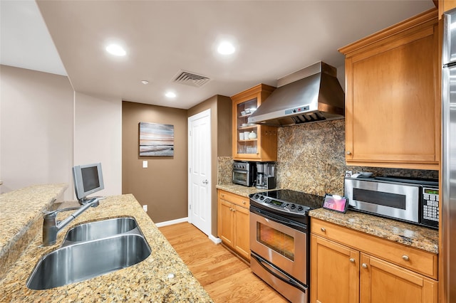 kitchen featuring a sink, range hood, appliances with stainless steel finishes, light stone countertops, and glass insert cabinets