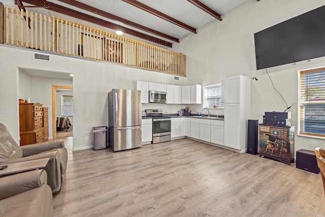 kitchen with white cabinets, beamed ceiling, stainless steel appliances, a high ceiling, and light wood-type flooring