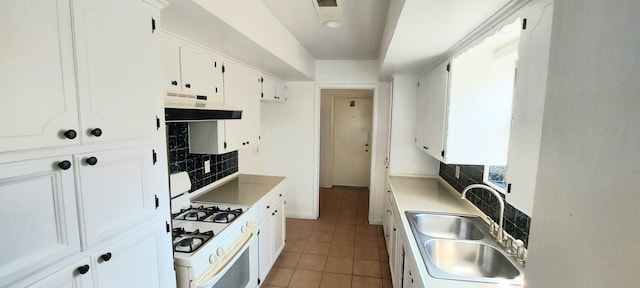 kitchen featuring white range with gas stovetop, sink, decorative backsplash, light tile patterned floors, and white cabinetry