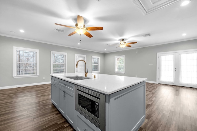 kitchen with dark hardwood / wood-style flooring, a kitchen island with sink, sink, gray cabinets, and stainless steel microwave