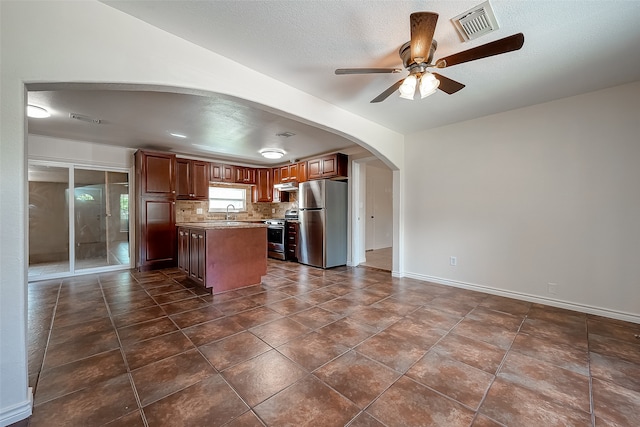 kitchen with ceiling fan, tasteful backsplash, a kitchen island, a textured ceiling, and appliances with stainless steel finishes