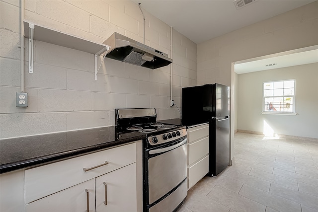 kitchen featuring stainless steel gas range, white cabinetry, black refrigerator, and light tile patterned floors