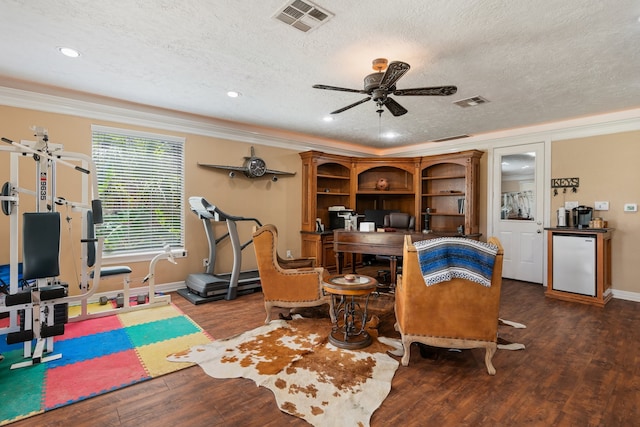 exercise area with a textured ceiling, crown molding, and dark wood-type flooring