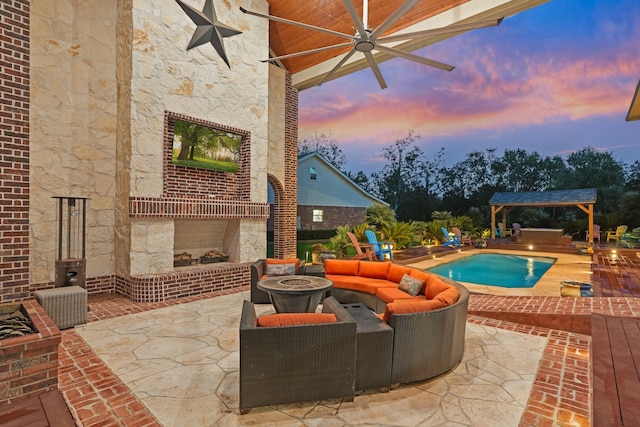 patio terrace at dusk with a gazebo, a swimming pool with hot tub, ceiling fan, and an outdoor living space with a fire pit