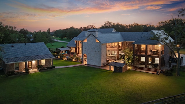 back house at dusk featuring a balcony and a lawn