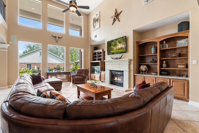 tiled living room featuring ceiling fan, a fireplace, a towering ceiling, and built in shelves