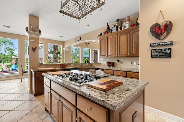 kitchen featuring a kitchen island, stainless steel gas stovetop, light tile patterned floors, and tasteful backsplash