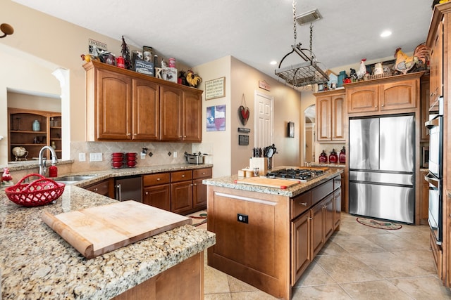 kitchen featuring an island with sink, stainless steel appliances, sink, pendant lighting, and backsplash