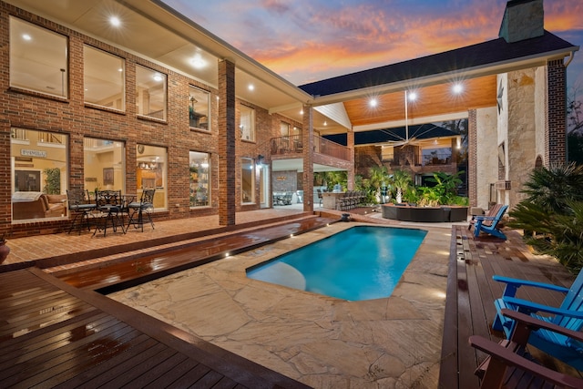 pool at dusk with a wooden deck and a patio