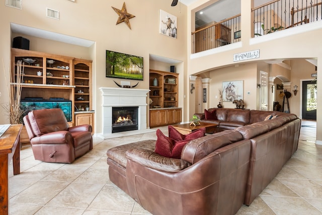 living room with a towering ceiling, built in shelves, decorative columns, and light tile patterned floors