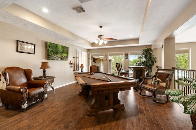 rec room featuring a textured ceiling, ceiling fan, dark wood-type flooring, and a raised ceiling