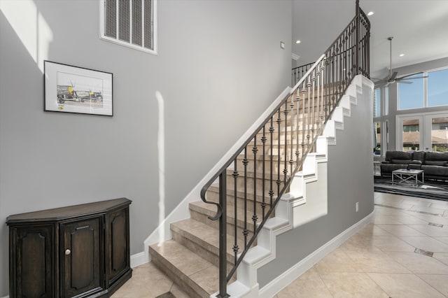 stairs featuring tile patterned floors, ceiling fan, and a towering ceiling