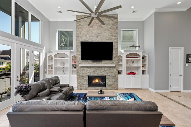 tiled living room with ceiling fan, a towering ceiling, a stone fireplace, french doors, and ornamental molding