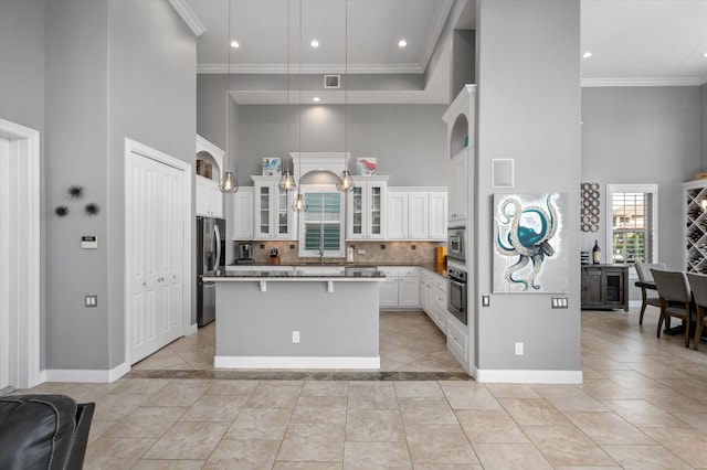 kitchen with hanging light fixtures, white cabinetry, appliances with stainless steel finishes, a high ceiling, and a kitchen bar