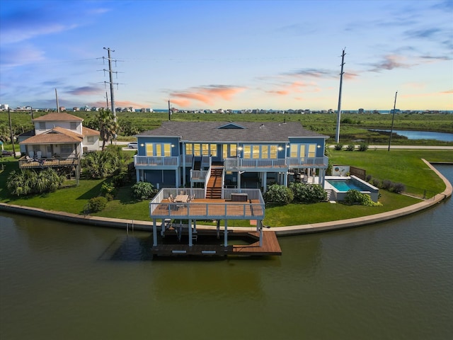 back house at dusk featuring a water view and a yard