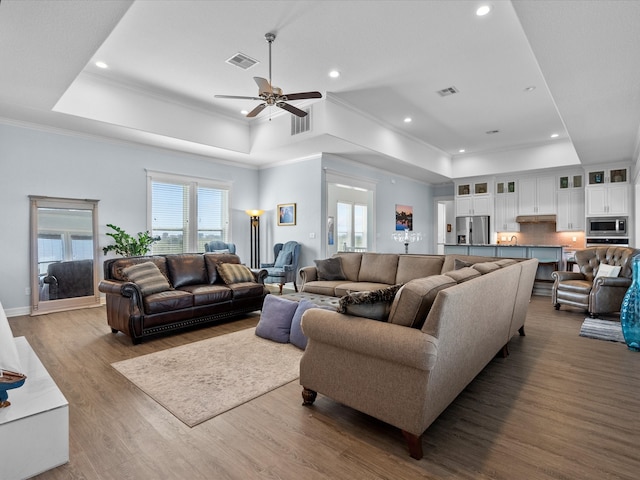 living room with wood-type flooring, a tray ceiling, crown molding, and ceiling fan