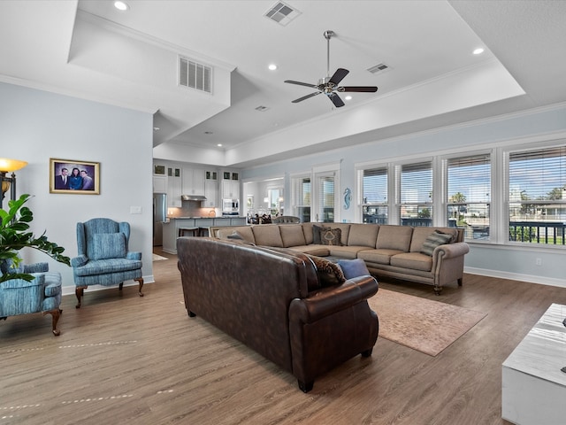 living room with ceiling fan, a raised ceiling, crown molding, and hardwood / wood-style floors