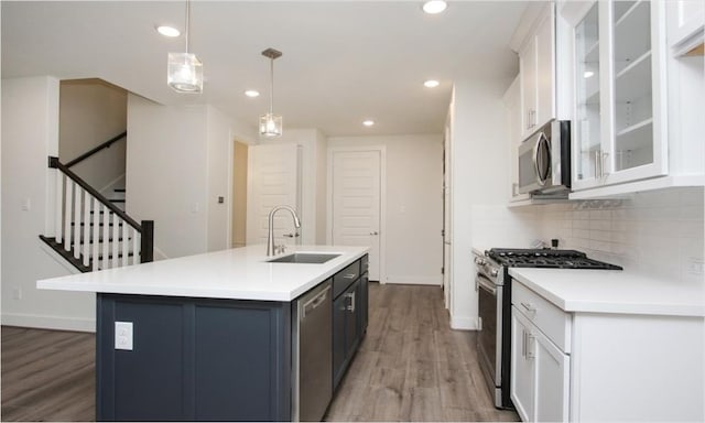 kitchen with pendant lighting, sink, white cabinetry, stainless steel appliances, and light hardwood / wood-style floors