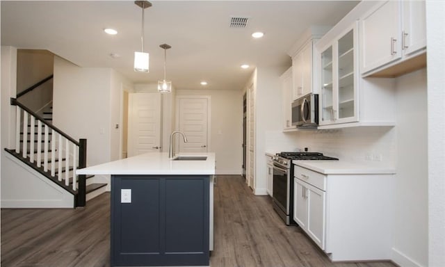 kitchen featuring dark hardwood / wood-style floors, stainless steel appliances, hanging light fixtures, white cabinetry, and a center island with sink