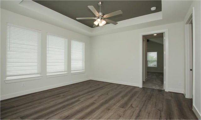 empty room featuring ceiling fan, a tray ceiling, dark hardwood / wood-style floors, and a wealth of natural light