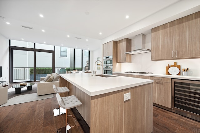 kitchen featuring wall chimney range hood, a center island with sink, wine cooler, dark hardwood / wood-style floors, and appliances with stainless steel finishes