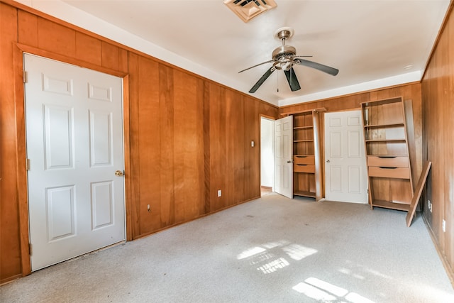 unfurnished bedroom featuring light carpet, ceiling fan, and wood walls