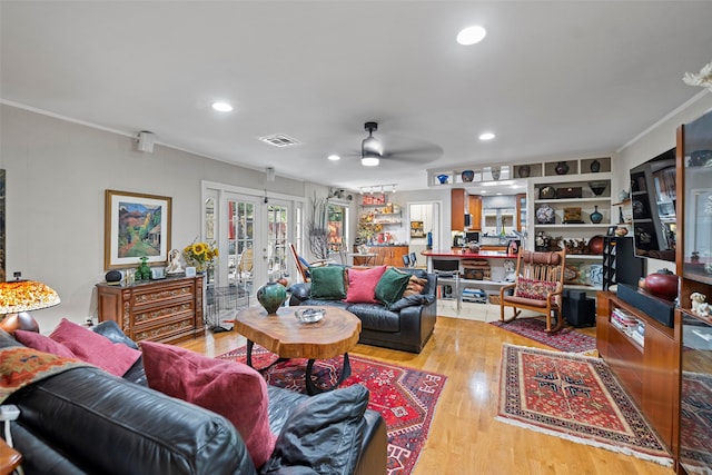 living room featuring ornamental molding, light wood-type flooring, ceiling fan, and french doors