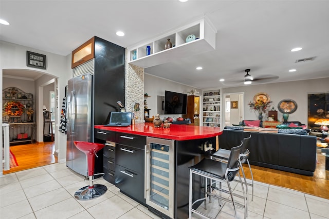 kitchen with ceiling fan, stainless steel fridge, beverage cooler, light hardwood / wood-style floors, and a kitchen breakfast bar