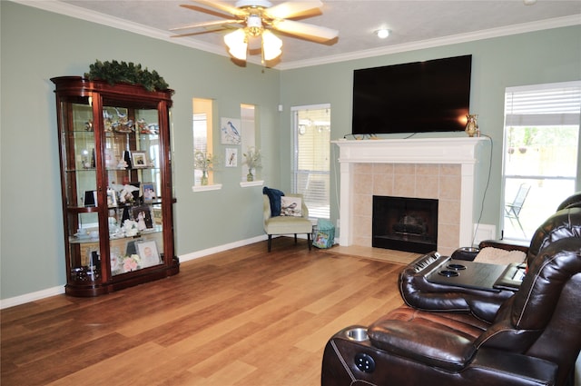 living room with hardwood / wood-style floors, ceiling fan, crown molding, and a tiled fireplace