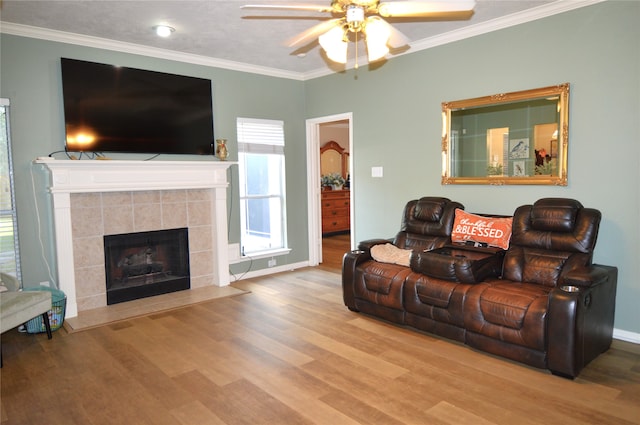 living room with crown molding, a fireplace, ceiling fan, and light wood-type flooring