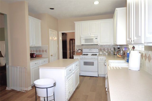 kitchen with white appliances, white cabinets, sink, tasteful backsplash, and a kitchen island