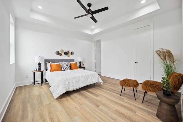 bedroom with ceiling fan, a tray ceiling, and light hardwood / wood-style floors