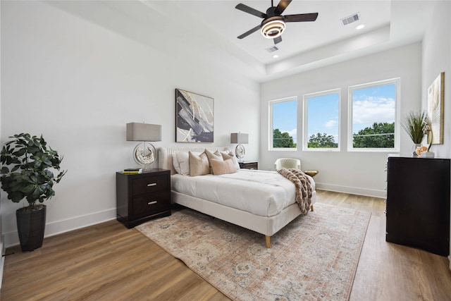 bedroom featuring wood-type flooring, a tray ceiling, and ceiling fan