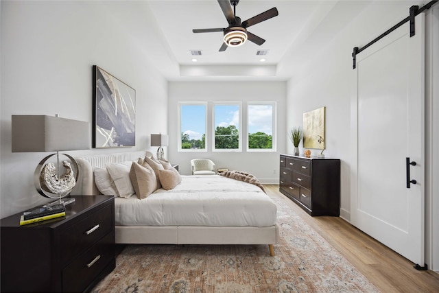 bedroom with a barn door, light hardwood / wood-style flooring, and ceiling fan