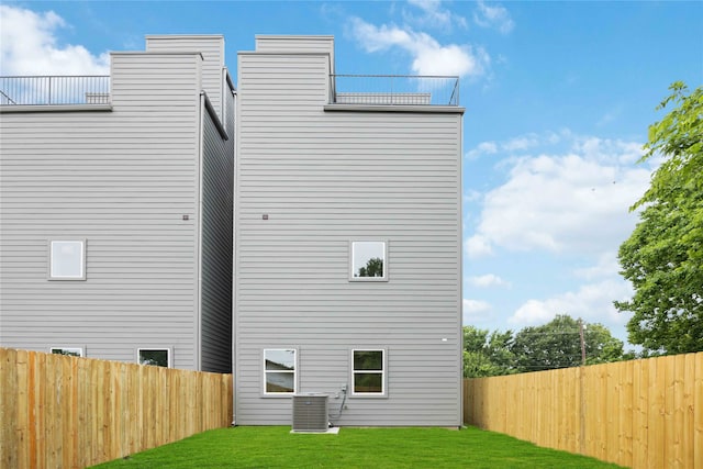 rear view of house featuring central AC unit and a lawn