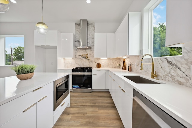 kitchen with wall chimney range hood, white cabinets, and appliances with stainless steel finishes