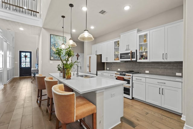 kitchen with sink, decorative light fixtures, white cabinets, a center island with sink, and high end appliances