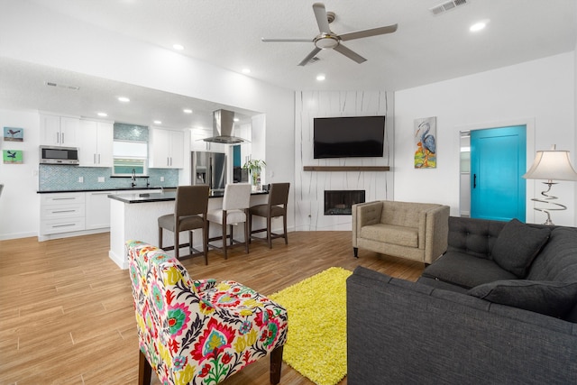 living room with ceiling fan, sink, a large fireplace, light hardwood / wood-style flooring, and a textured ceiling