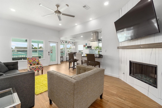 living room featuring ceiling fan, a textured ceiling, and light hardwood / wood-style flooring