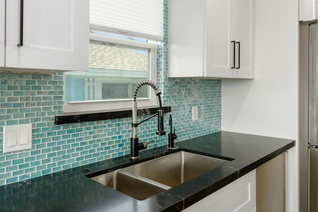 kitchen with stainless steel refrigerator, dark stone countertops, sink, decorative backsplash, and white cabinetry