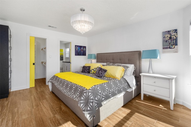 bedroom with a spacious closet, hardwood / wood-style floors, a chandelier, and ensuite bath