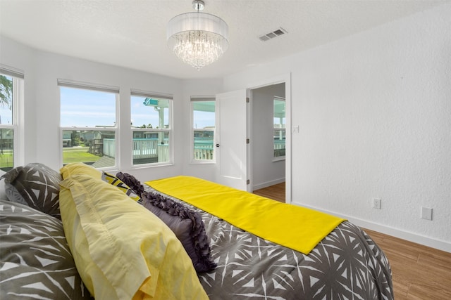 bedroom featuring wood-type flooring, a notable chandelier, multiple windows, and a textured ceiling