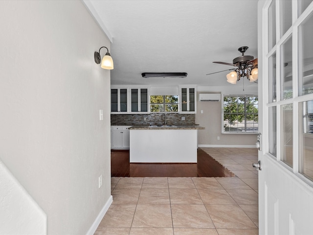 kitchen with backsplash, a wall mounted air conditioner, light tile patterned floors, and white cabinetry