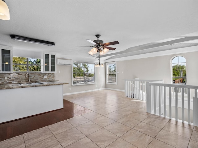 interior space featuring light wood-type flooring, ceiling fan with notable chandelier, sink, a wall mounted air conditioner, and a textured ceiling