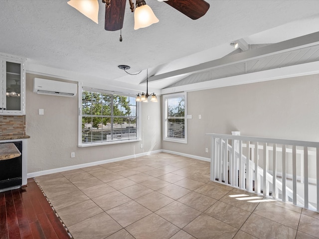 interior space featuring light wood-type flooring, ceiling fan with notable chandelier, a wall mounted air conditioner, vaulted ceiling with beams, and a textured ceiling