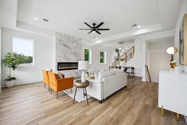 living room featuring ceiling fan, light wood-type flooring, a tray ceiling, and a high end fireplace