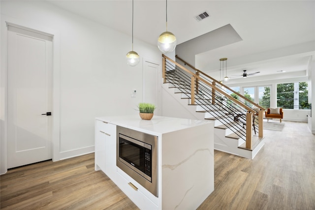 kitchen featuring light stone counters, white cabinets, decorative light fixtures, light hardwood / wood-style flooring, and stainless steel microwave