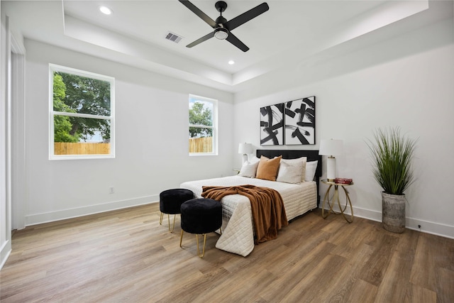 bedroom with multiple windows, ceiling fan, hardwood / wood-style floors, and a raised ceiling