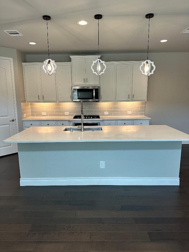 kitchen with a sink, stainless steel microwave, a center island with sink, and light countertops